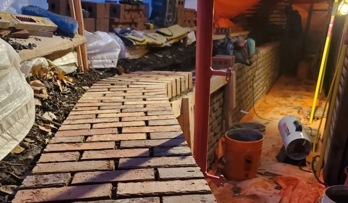 A partially constructed brick wall with tools, buckets, and construction materials scattered around the work area.