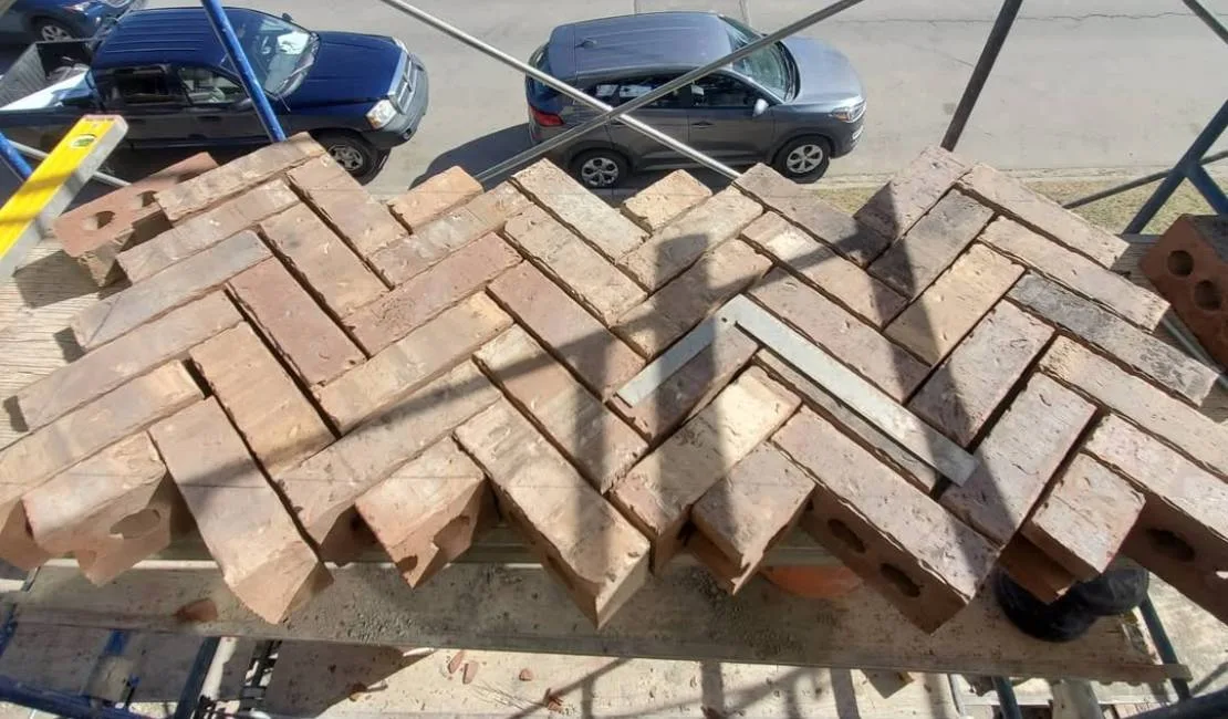 Bricks arranged in a herringbone pattern on a wooden surface, with cars visible on the street below.