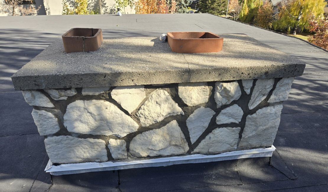 A stone chimney with two rectangular clay chimney flue liners on top, situated on a flat roof.