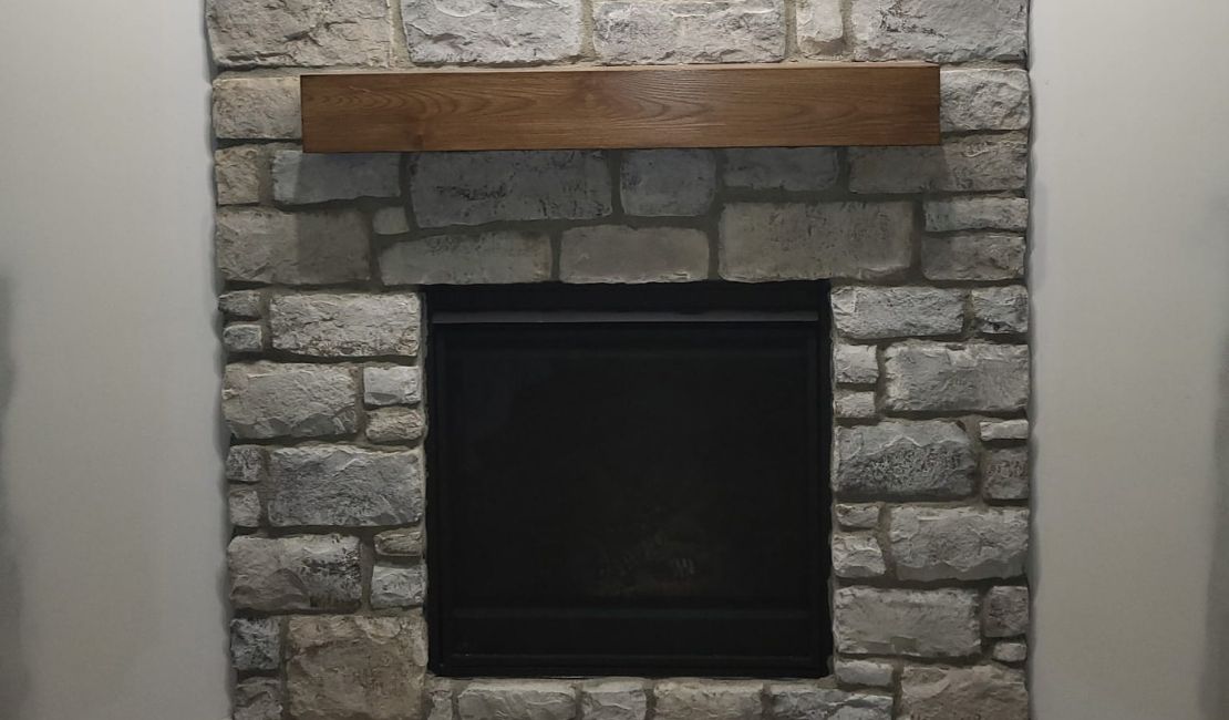 Stone fireplace with a wooden mantel against a light-colored wall.