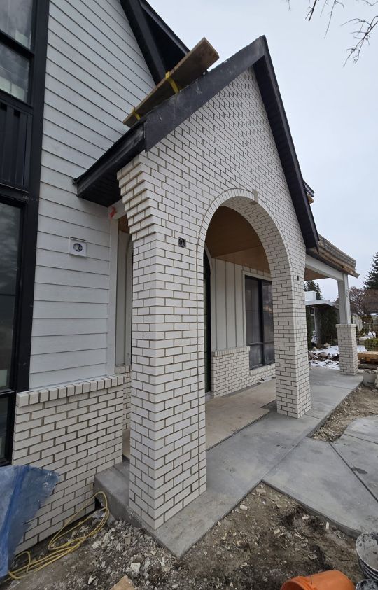 White brick archway and columns at the entrance of a house under construction, with unfinished landscaping visible in the foreground.