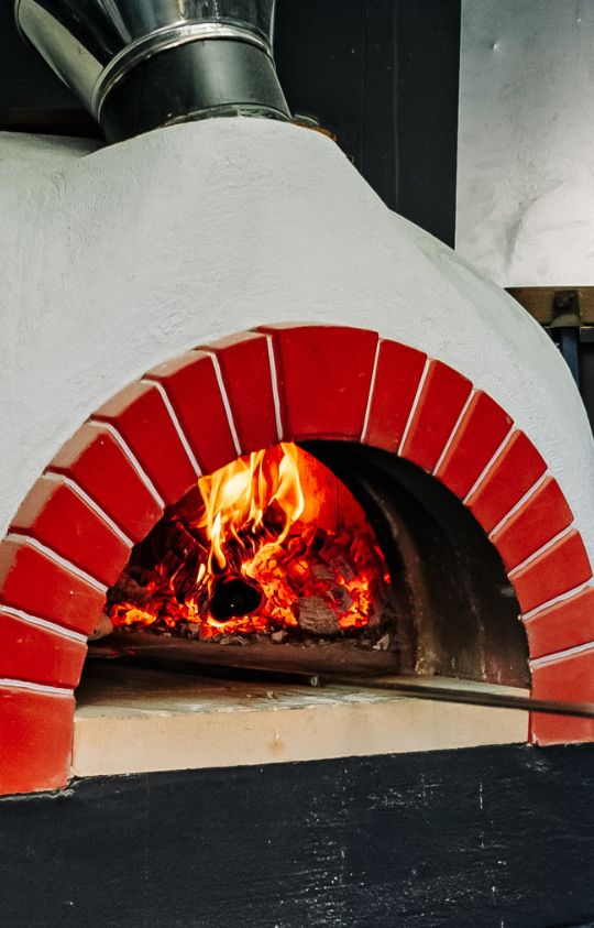 A wood-fired pizza oven with red brick trim and visible flames and glowing embers inside.