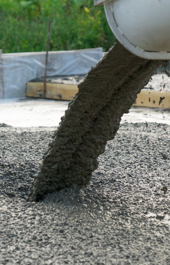 Wet concrete pouring from a chute onto a construction site foundation.