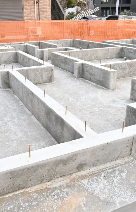 Concrete foundation with embedded metal rods outlining the base structure for a building under construction.
