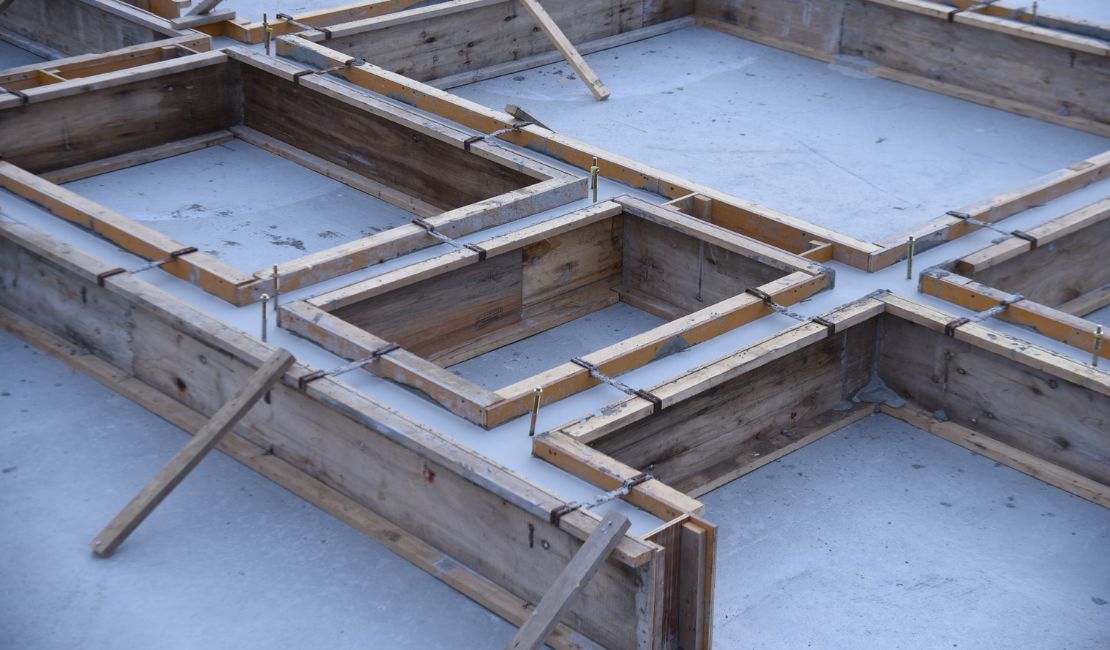 Wooden formwork arranged in geometric shapes on a concrete slab foundation at a construction site.