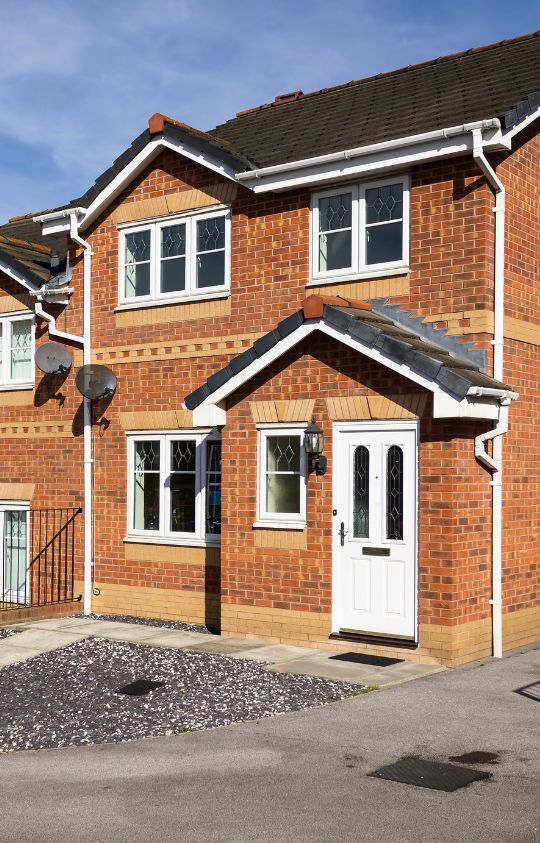 Homepage – 1 A modern red brick house with white-framed windows, a white front door, and a small gravel yard.