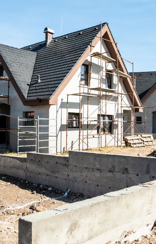 Homepage – 2 Modern house under construction with scaffolding around the exterior and unfinished concrete walls in the foreground.