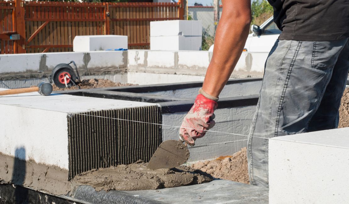 Homepage A construction worker laying white concrete blocks with mortar, using a trowel and aligning them with a taut guide string.