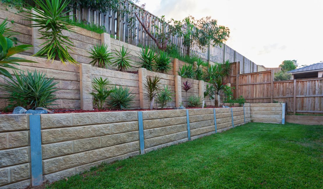 Tiered garden with stone retaining walls, neatly trimmed grass, and a variety of green and spiky plants on different levels.