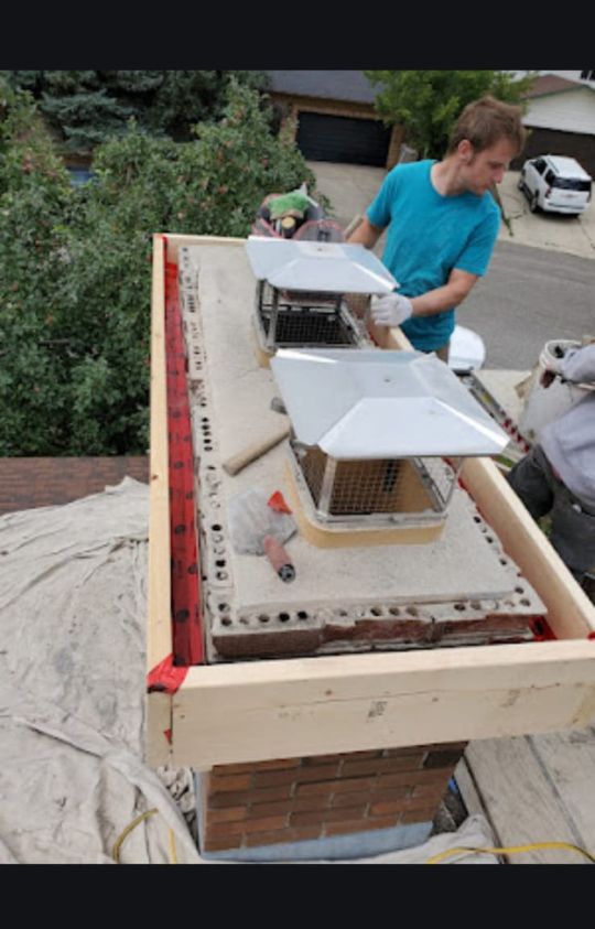 A person in work clothes is installing metal chimney caps on top of a brick chimney, with tools and materials laid out nearby.