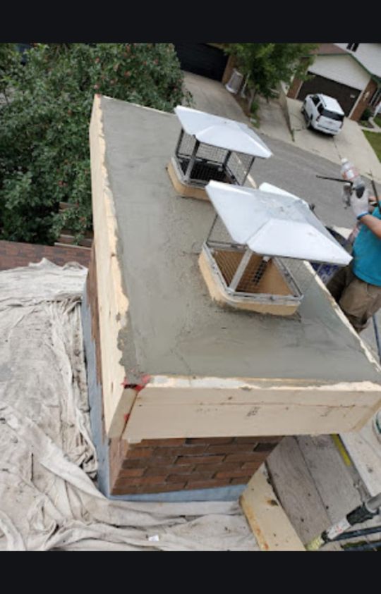 A freshly repaired chimney top with two metal caps, surrounded by scaffolding and protective sheets, overlooking a residential street.