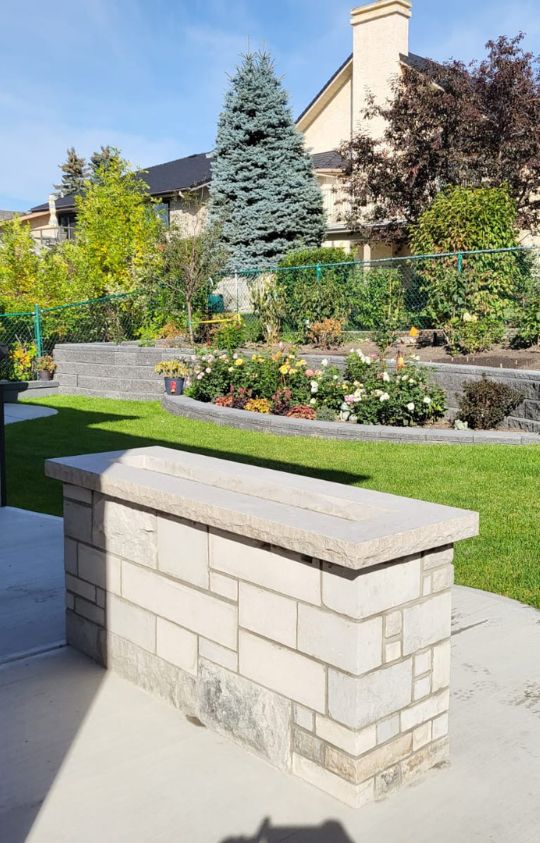 custom outdoor gallery potrait 2 Stone planter box on a patio, with a well-maintained garden, green lawn, and residential houses in the background.
