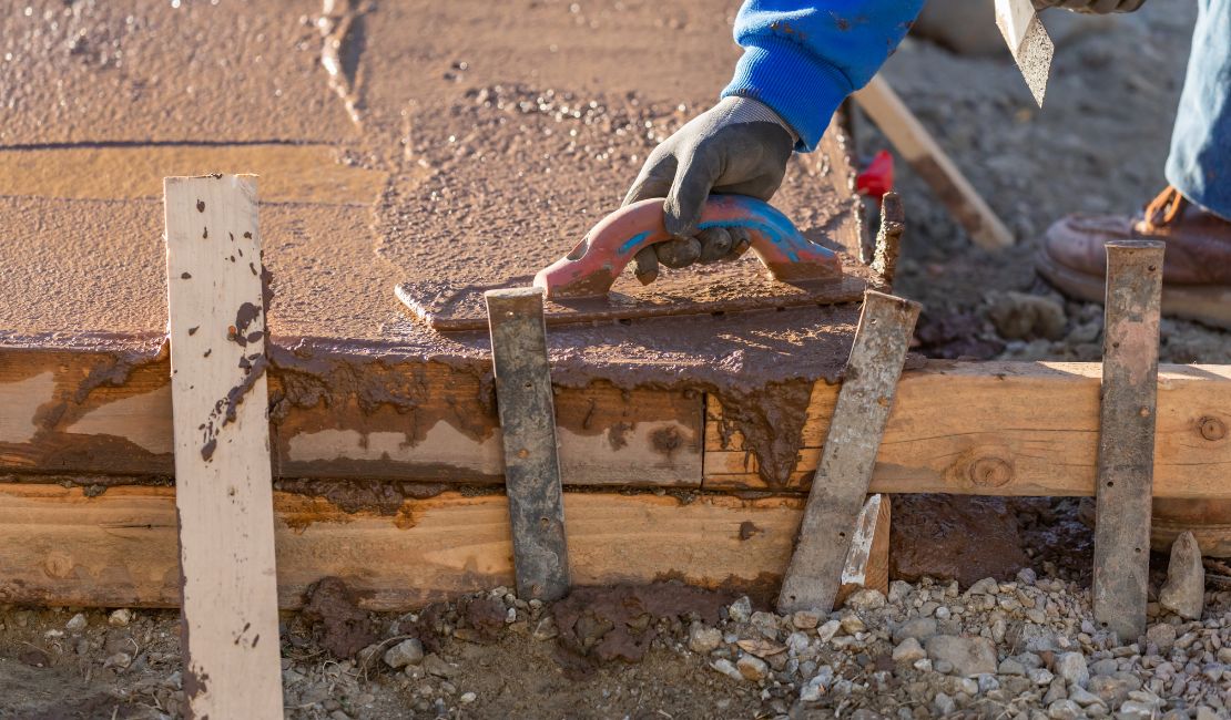 A person wearing gloves smooths wet concrete on a wooden formwork at a construction site.
