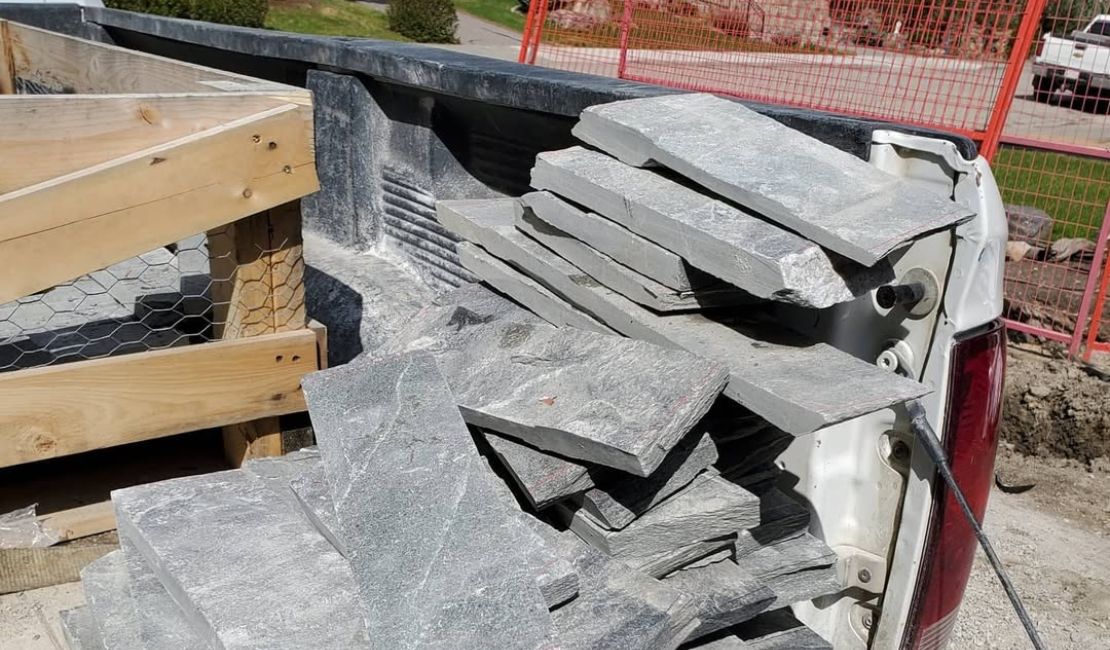 Several large, flat stone slabs are stacked in the back of a pickup truck at a construction site.