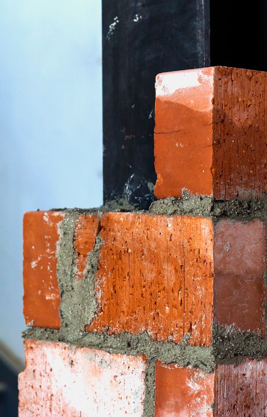 A close-up of red bricks stacked with gray mortar, partially built around a black metal beam.