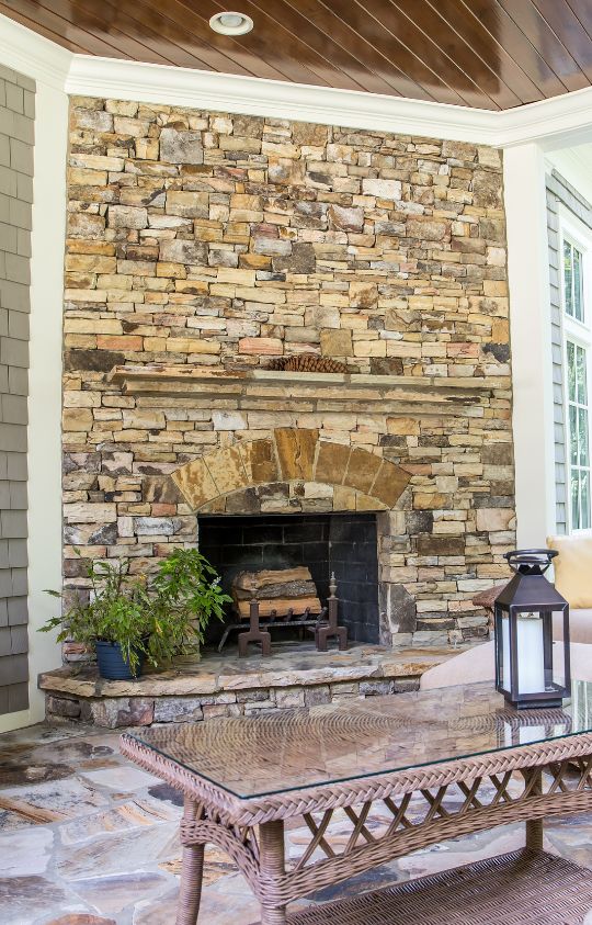Stone fireplace with a black metal grate and small plant beside it, a wicker table with a lantern in the foreground.